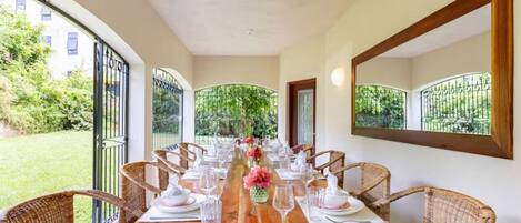 A dining area with a long wooden table set for six, surrounded by wicker chairs.
