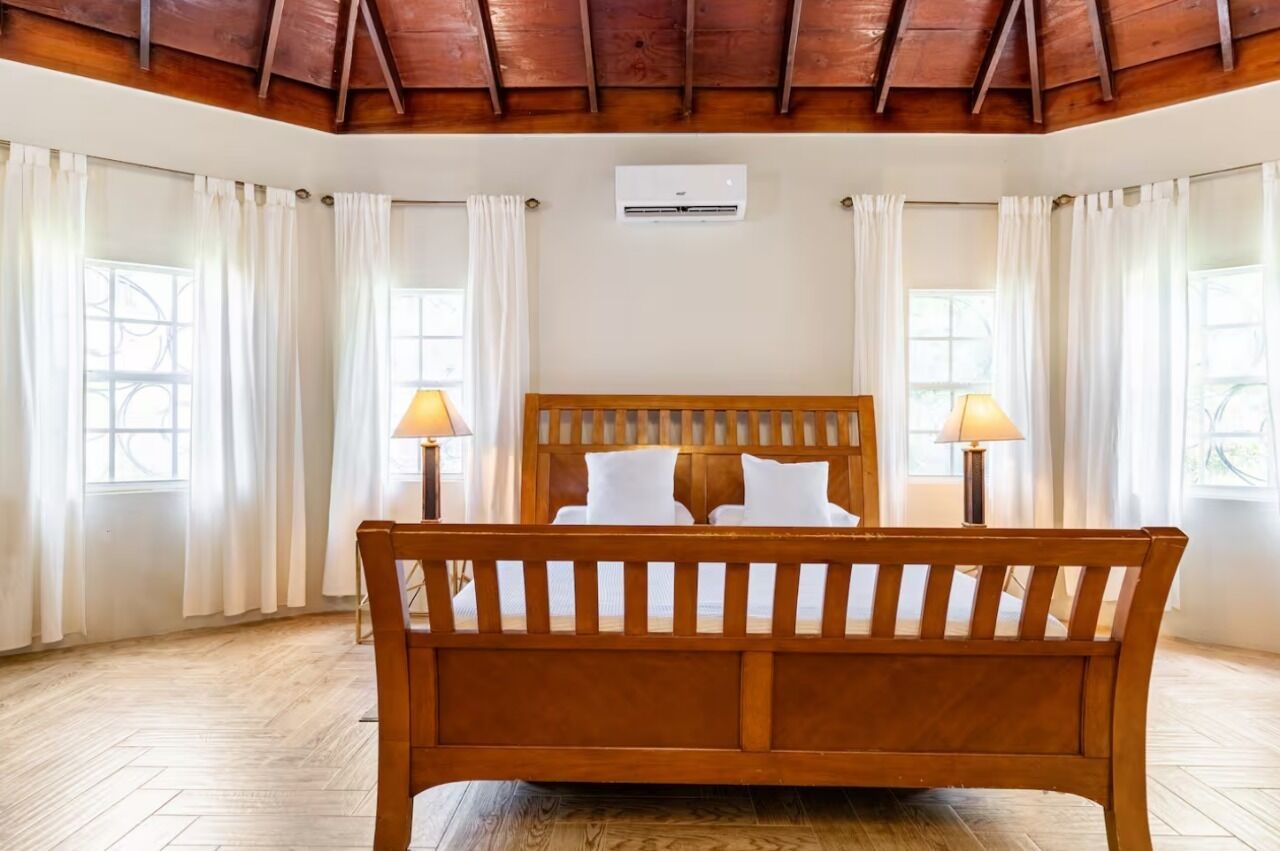 Un dormitorio con cama de madera, cortinas blancas y piso de madera.