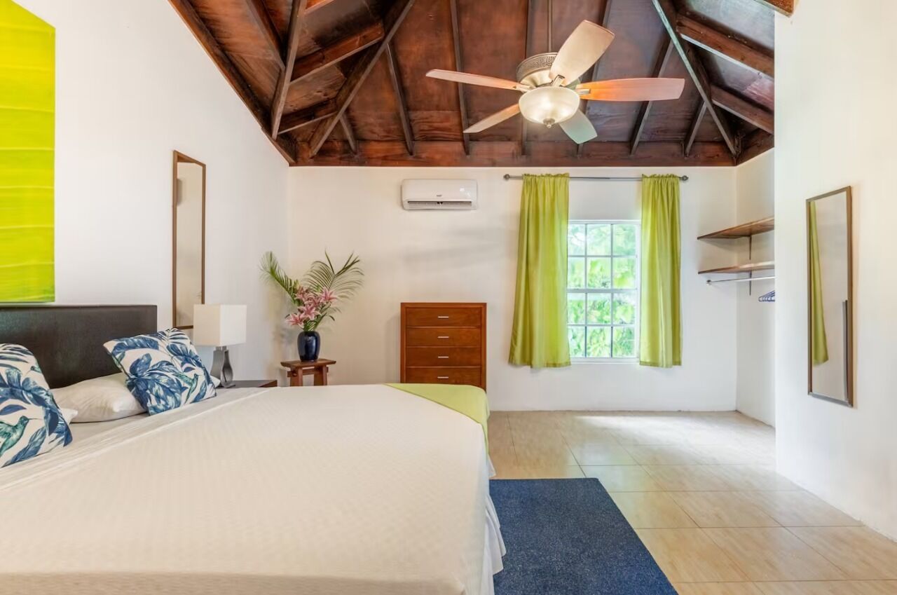 Un dormitorio con una cama grande, un ventilador de techo, una ventana con cortinas verdes y un techo de madera.