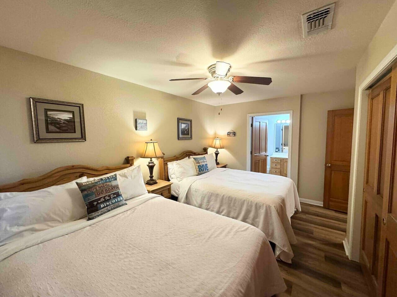 Habitación de hotel con dos camas, un ventilador de techo y una puerta que da a otra estancia.