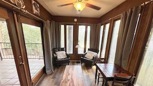 Ein Zimmer mit Holzboden, zwei Ledersesseln, einem Holztisch und einem Deckenventilator.