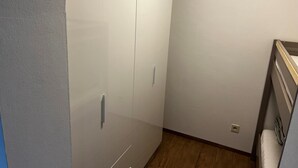 A narrow hallway with a white wardrobe, a wooden floor, and a bed with a striped pillow. - Vacation apartment in Prien am Chiemsee (Prien am Chiemsee)