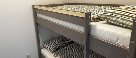 A bunk bed with striped bedding in a room with plain walls and wooden flooring.