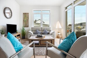 Un salon moderne avec un canapé, une table basse et un téléviseur, une grande fenêtre offrant une belle vue et une horloge au mur.
