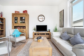 A living room with a sofa, a coffee table, a TV stand, a wooden cabinet, and a wall clock.