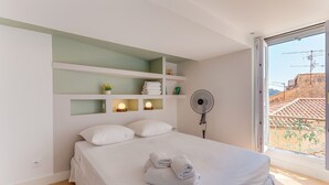 A bedroom with a bed, a fan, a window, and a view of buildings. - AUTHENTIC VILLEFRANCHE AP4472 By Riviera Holiday H (Villefranche-sur-Mer)