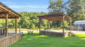 A covered outdoor area with a wooden deck, picnic tables, and a pergola.