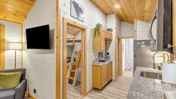 Un espace de vie compact comprenant un coin cuisine, un téléviseur fixé au mur et un petit coin salon.