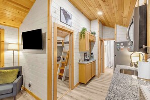 Un espacio habitable compacto con kitchenette, televisor montado en la pared y una pequeña zona de estar.