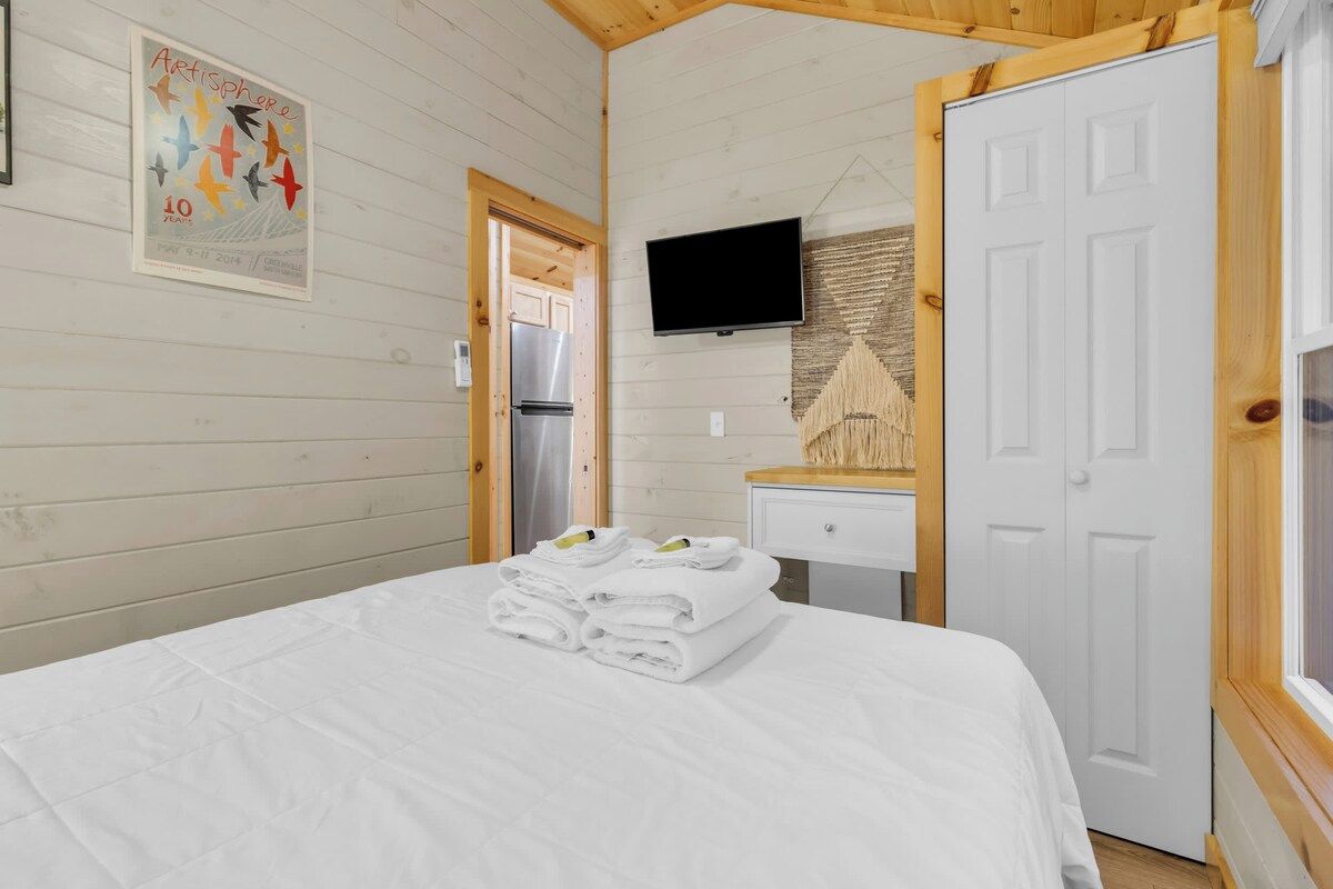 A hotel room with a bed, a television, a door, and a poster on the wall.