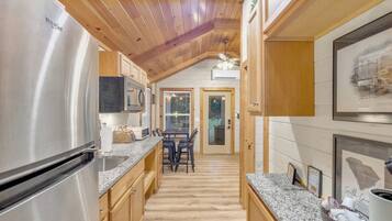A kitchen with wooden cabinets, a stainless steel refrigerator, granite countertops, and a dining area with a table and chairs.