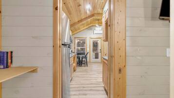 A narrow hallway with wooden walls and a sloped ceiling, leading to a dining area with a table and chairs.