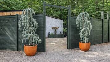 Une entrée fermée par un portail, avec deux arbres en pot de chaque côté et un bâtiment en arrière-plan.