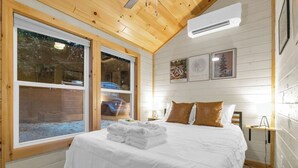 Ein gemütliches Schlafzimmer mit einem großen Bett, Holzwänden und einem Fenster mit Blick auf eine verschneite Landschaft.