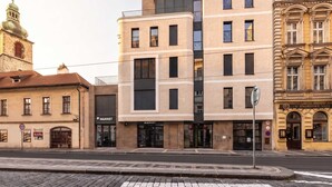 En byggnad med flera våningar, en modern fasad, en tydligt markerad entré och en gatufasad med en trottoar av kullersten.