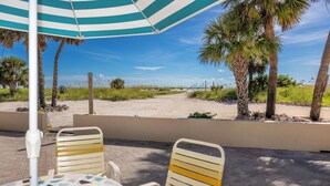 A beachside patio with a striped umbrella, two chairs, and a table with a mosaic tile pattern. - Beachside at Birdsong #17 Pool 5 Steps to the Sand (Treasure Island)