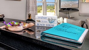 A reception desk with a 'Welcome to our Beach House' sign, a guest information booklet, and a decorative shell basket. - Beachside at Birdsong #17 Pool 5 Steps to the Sand (Treasure Island)
