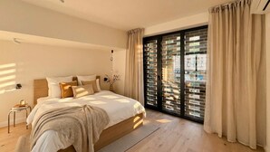 A modern bedroom with a large bed, a small bedside table, a nightstand, and a view through a sliding glass door. - TurnKey | Henry's Tower Apartment II-3 (Hlavní město Praha)