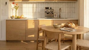 A modern kitchen with wooden cabinets, a built-in coffee machine, and a round dining table with wicker chairs. - TurnKey | Henry's Tower Apartment II-3 (Hlavní město Praha)