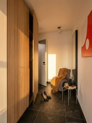 A modern interior with a wooden wardrobe, a seating area with a cushion and a plant, and a tiled floor. - TurnKey | Henry's Tower Apartment II-4 (Hlavní město Praha)