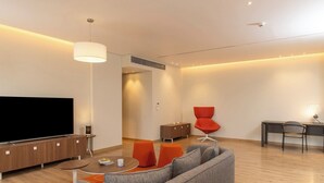 Una sala moderna con un televisor de pantalla plana, un sofá, una mesa de centro y una zona de comedor con una silla y un escritorio.