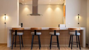 Una cocina moderna con una isla central, cuatro taburetes de bar e iluminación colgante.