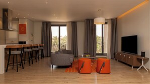 Una sala de estar moderna con un sofá, otomanas, un televisor y un comedor con sillas y una mesa.