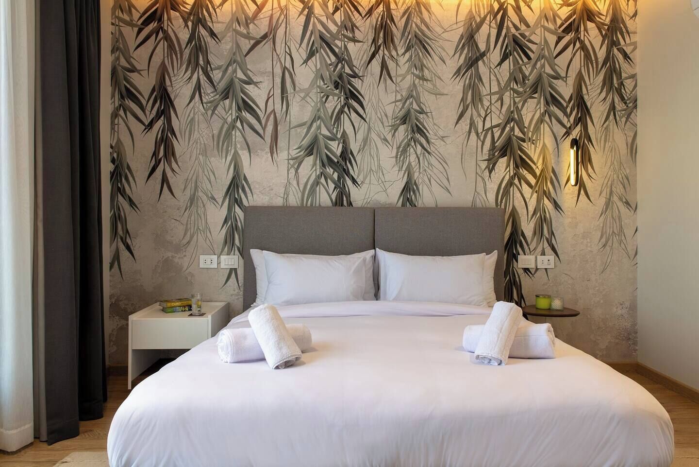 Een hotelkamer met een groot bed, twee nachtkastjes en een wand met een bamboebladmotief.