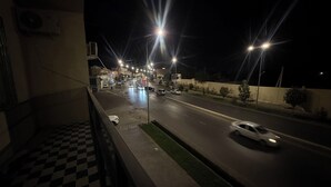 Szenischer Blick von einem Balkon bei Nacht: ein Schachbrettmuster auf dem Boden, Straßenlaternen und Autos auf der Fahrbahn.