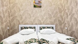 Een tweepersoonsbed met witte lakens en kussens met camouflageprint, voor een behang met bladmotief.