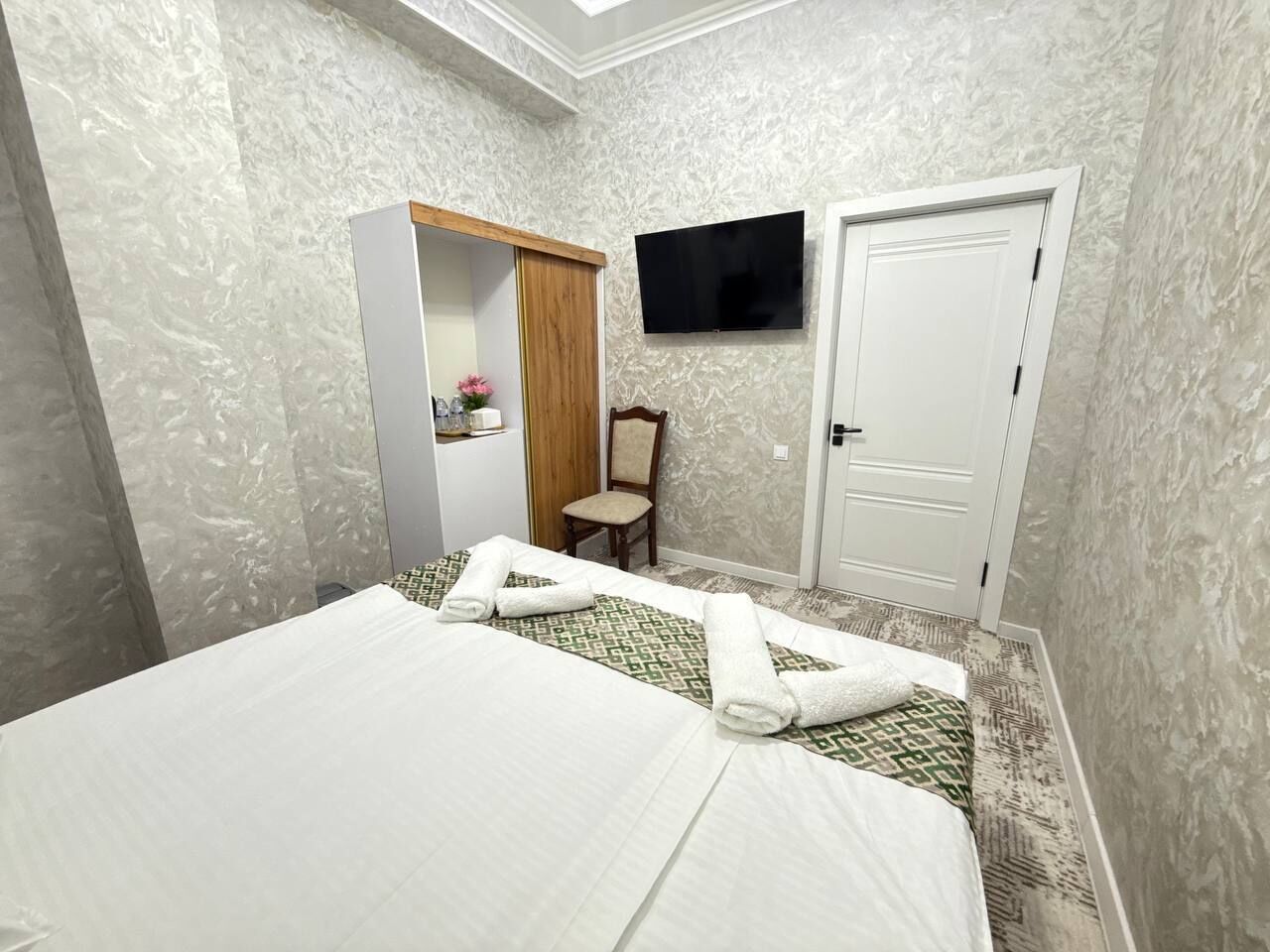 Et hotelværelse med seng, garderobeskab, fjernsyn og stol.