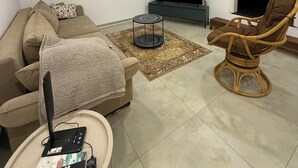 Een moderne woonkamer met een bank, een rieten stoel, een televisie en een tafeltje met elektronische apparaten.
