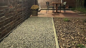 Een gebouw van baksteen met een terras, compleet met een tafel en stoelen, omgeven door grind en houtsnippers.