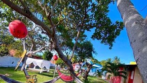 A hammock tied between trees in a grassy area with a clear blue sky. - Pousada Estrela Mar  (Jandaira)