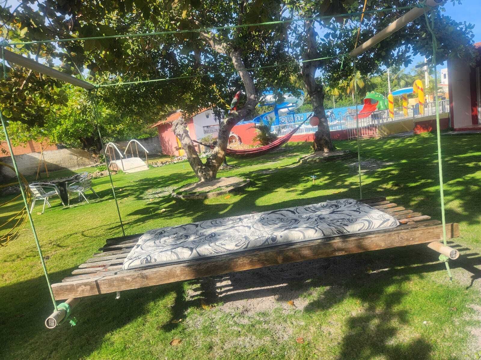 A hammock suspended between trees in a grassy area with a wooden bench and a swing set.