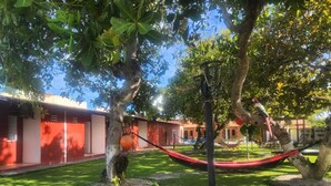 A courtyard with a hammock, trees, and a building with red walls and windows. - Pousada Estrela Mar  (Jandaira)