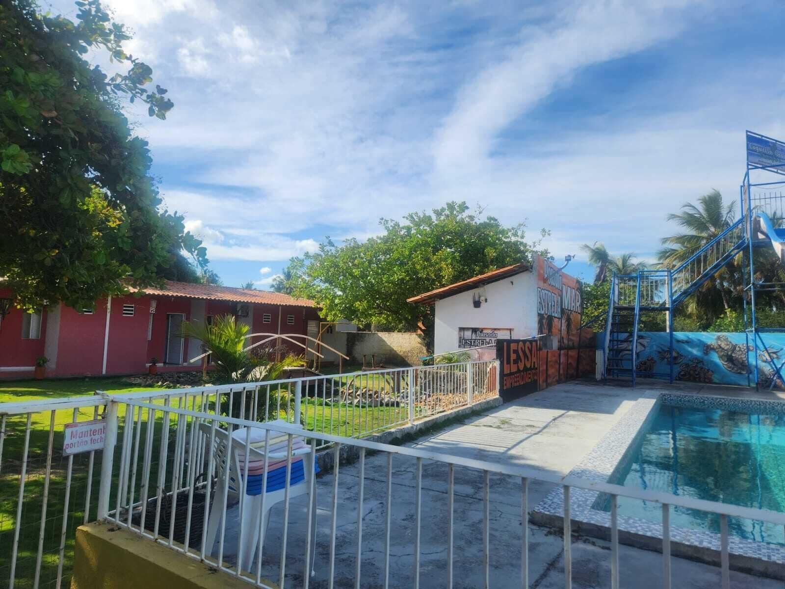 A swimming pool area with a fenced deck, a small building, and a mural.