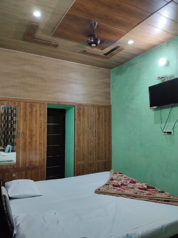 A bedroom with a bed, wooden wardrobe, green walls, ceiling fan, and a mounted TV. - Hotel Comfort Zone (Thanesar)