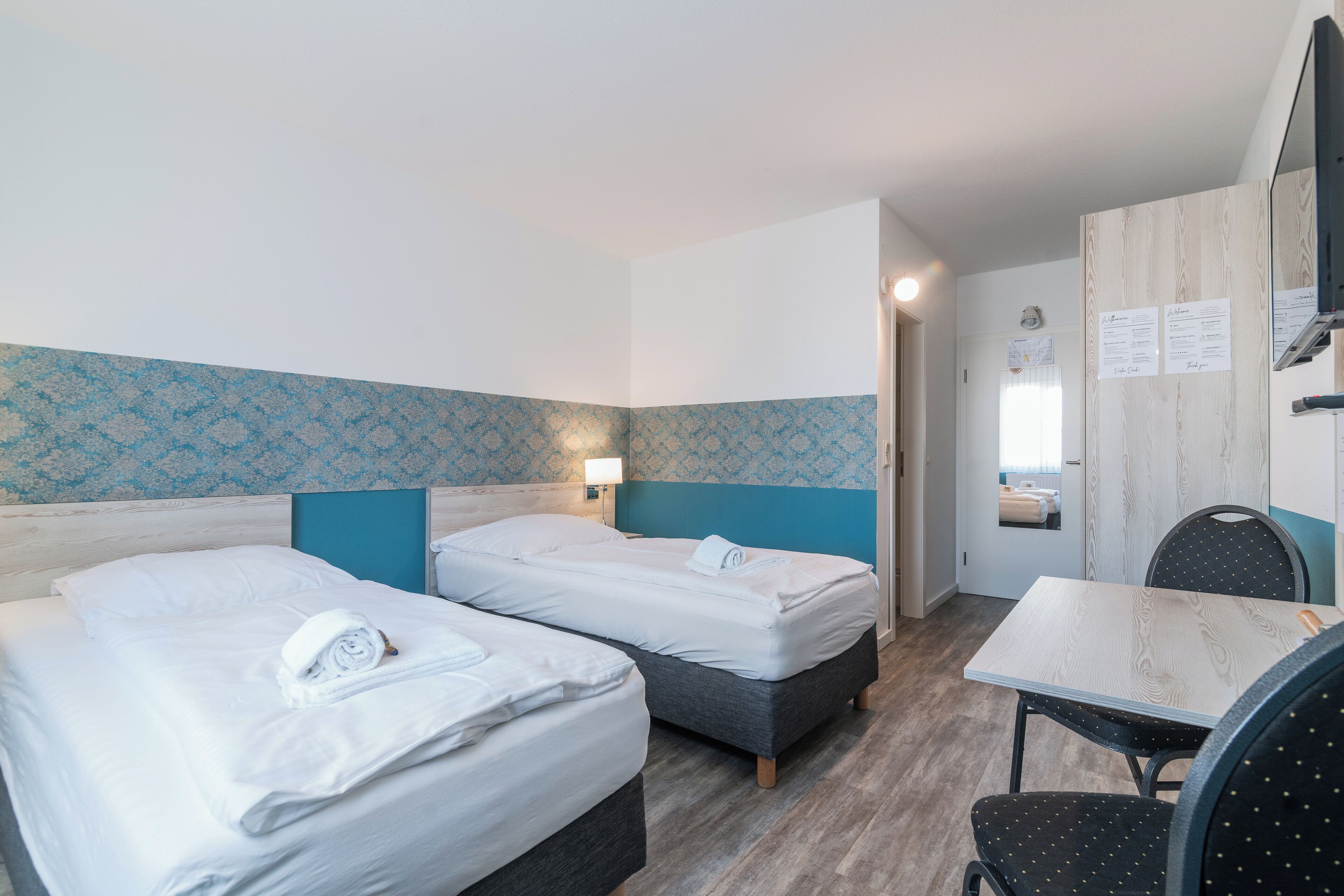 A hotel room with two beds, a desk, and a chair.