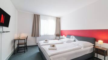 A hotel room with two beds, a desk, a TV, and a window with curtains.