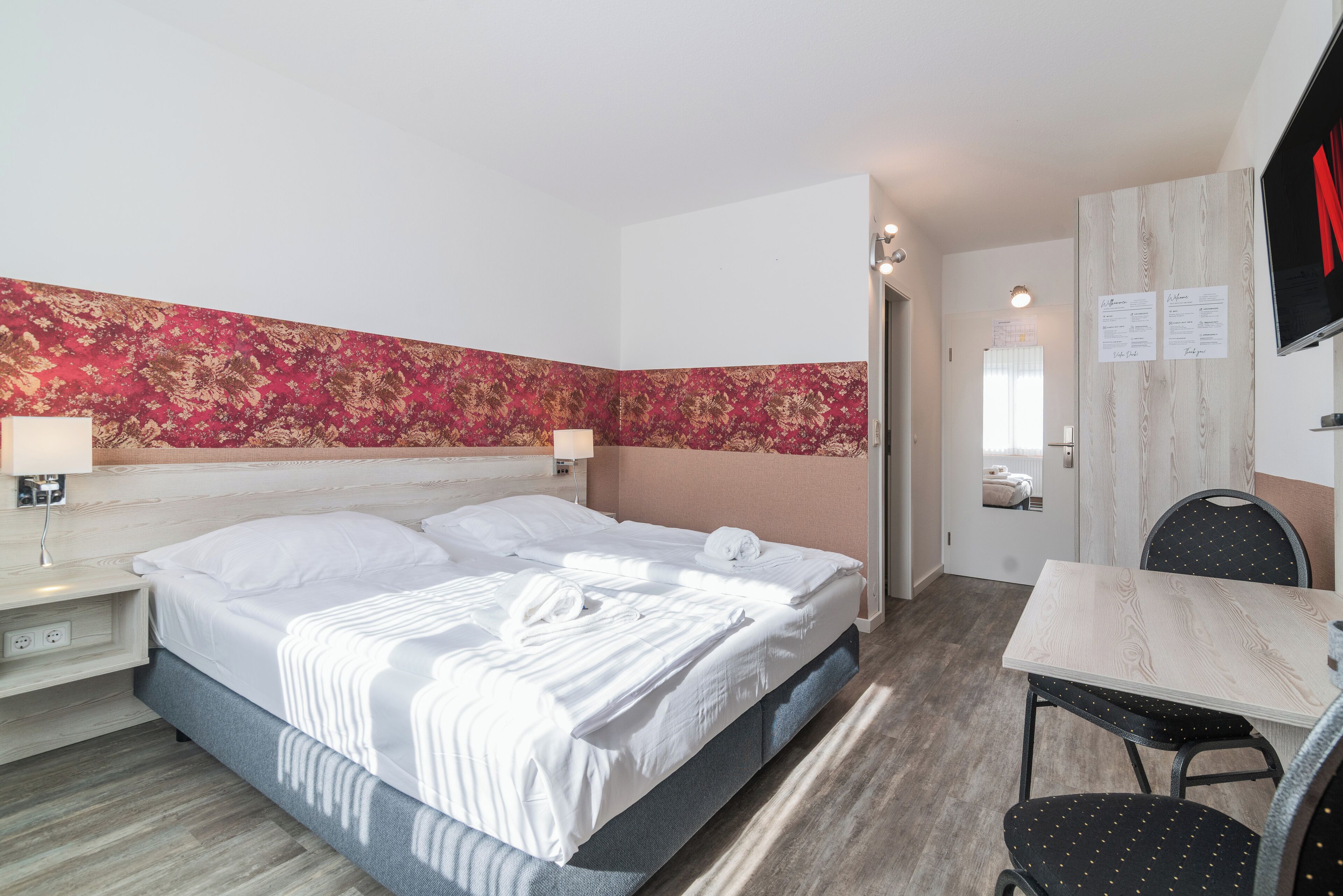 A hotel room with a bed, bedside table, lamp, and a desk with a chair.