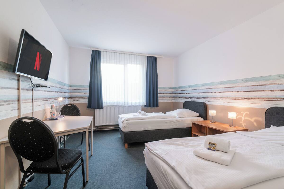 Ein Hotelzimmer mit Bett, Schreibtisch, Stuhl, Fernseher und einem fenster mit Vorhängen.