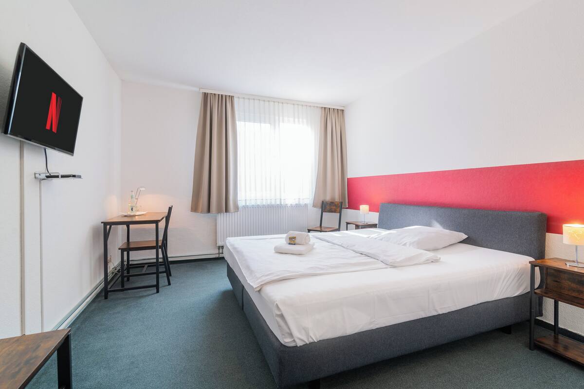 Ein Hotelzimmer mit einem Bett, einem Schreibtisch, einem Sessel, einem Fernseher und einem Fenster mit Vorhängen.