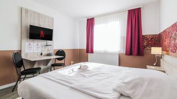 Ein Hotelzimmer mit Bett, Schreibtisch mit Fernseher, Stuhl, Fenster mit Vorhängen und einer Wand mit dekorativem Wandpaneel.