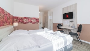 Hotelkamer met een bed, bureau, stoel, televisie en een bloemenpatroon op de muur.