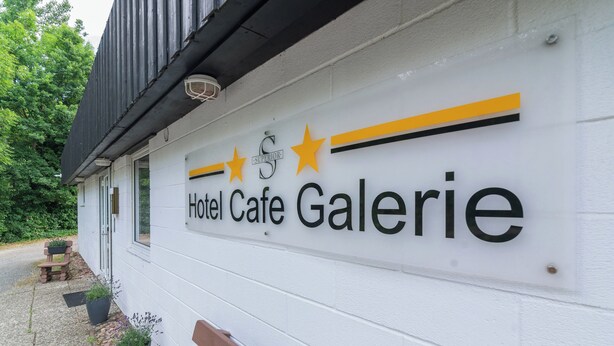 Een bord voor Hotel Café Galerie, met een modern ontwerp, met sterren en het woord 'Superior' boven de naam.