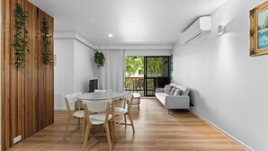 A modern living room with a round dining table, white chairs, a grey sofa, and a wooden partition with plants. - Beachside Bliss on Palm Avenue (Surfers Paradise)