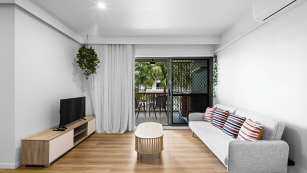 A modern living room with a grey sofa, a wooden TV stand, and a round ottoman. - Beachside Bliss on Palm Avenue (Surfers Paradise)