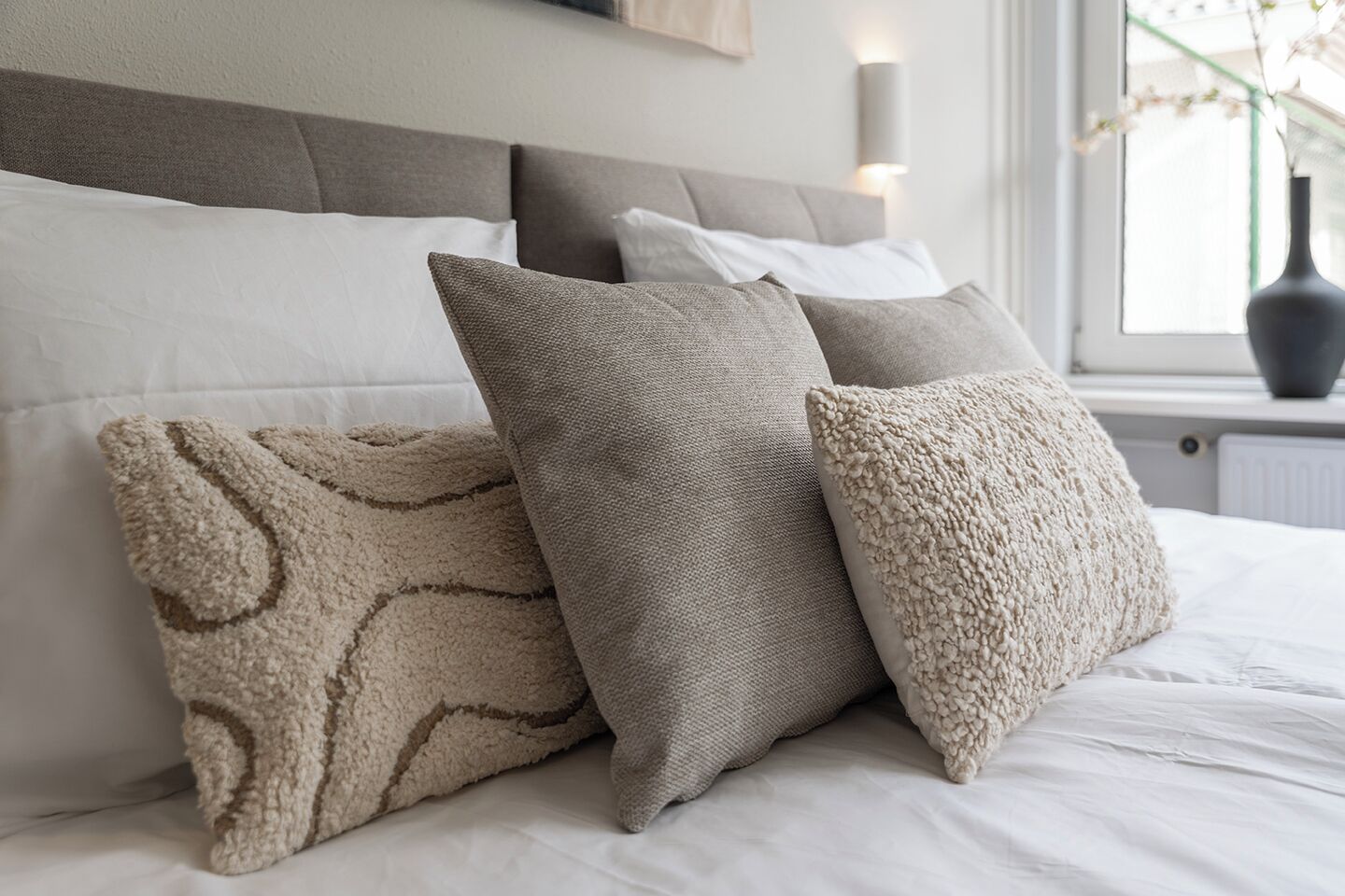 A bed with white bedding and three pillows in a neutral color scheme.