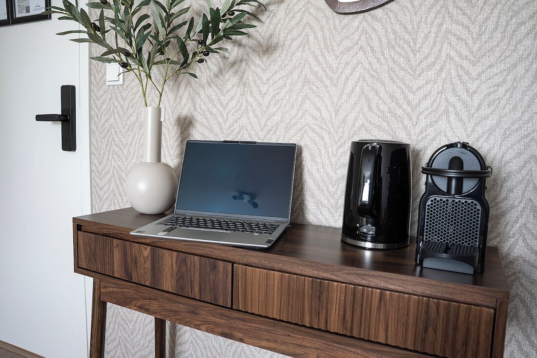 A laptop on a wooden desk with a vase of green leaves and a black speaker.